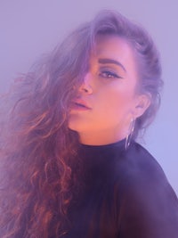 a woman with long curly hair posing in front of a purple background